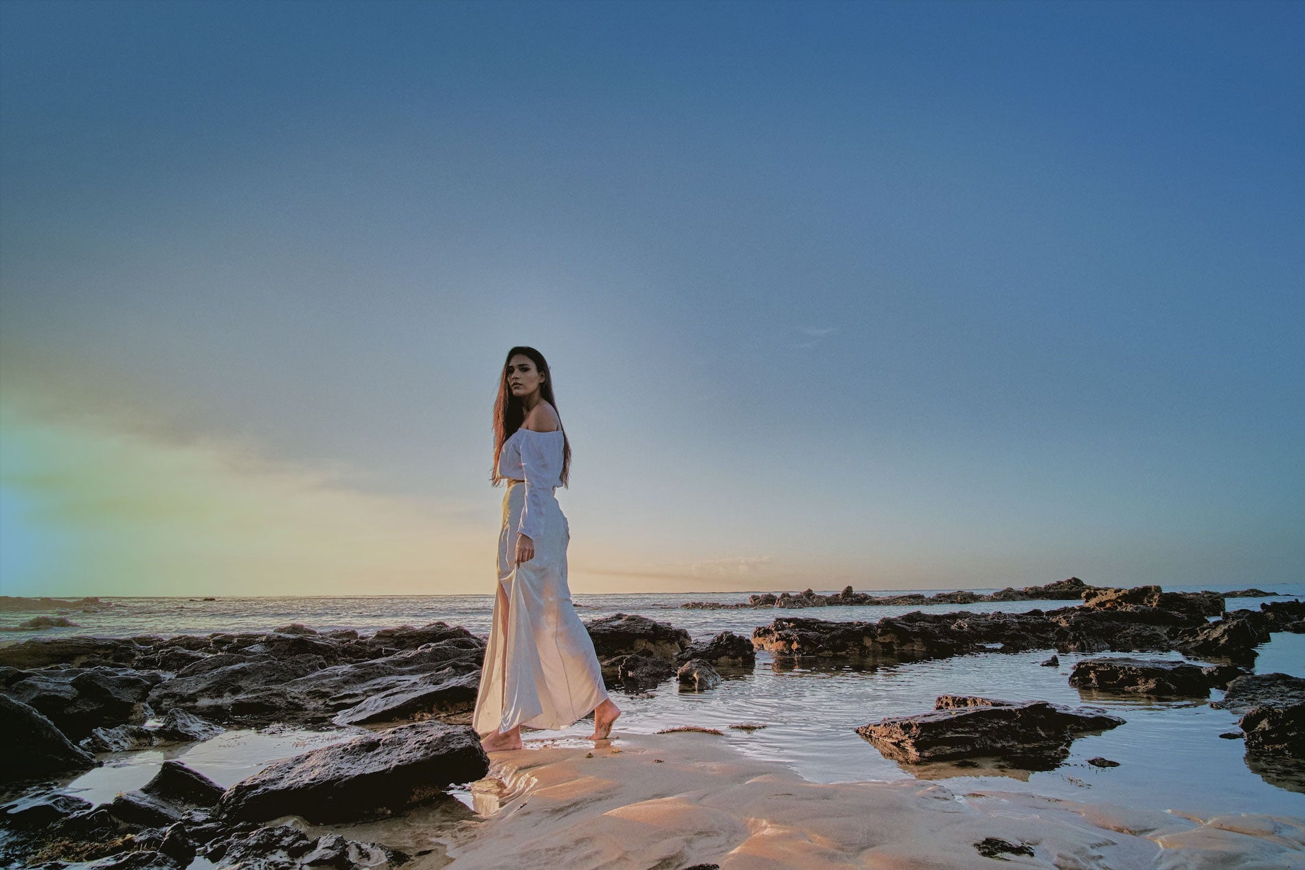 Women in white dress walking on sand and rocks at the beach